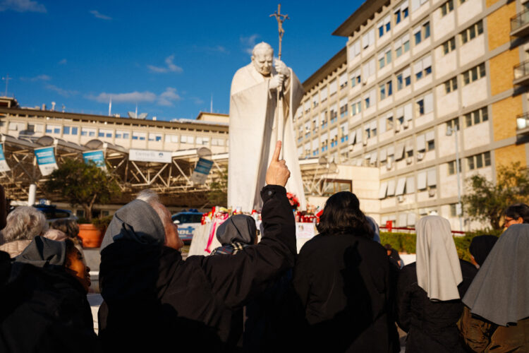 Fieles católicos oran por el papa Francisco al pie de la estatua de Juan Pablo II, en Roma.