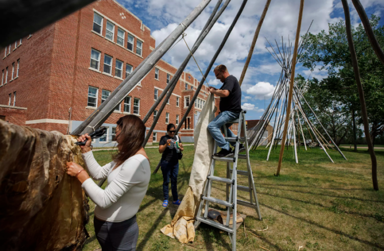 Estudiantes fijan una piel de alce a un tipi fuera de la universidad Nuhelt'ine Tahiyots'i Nistameyimakanak Blue Quills, en St. Paul, Alberta, Canadá. Foto: AFP.