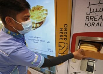 Un hombre agarra el pan gratis de uno de los dispensadores. Foto: AFP.