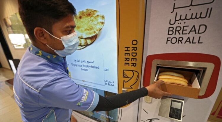 Un hombre agarra el pan gratis de uno de los dispensadores. Foto: AFP.