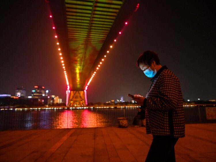 Una mujer mira su teléfono móvil el 9 de noviembre de 2022 bajo el puente Lupu de Shanghái. Foto: AFP.