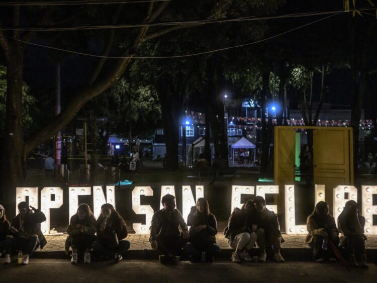 Personas sentadas frente a un cartel del Open San Felipe en Bogotá, el 3 de diciembre de 2022. Foto: AFP.