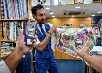 El sastre Roshan Melwani habla con un cliente mientras su equipo lo graba en el negocio Sam's Tailor de Hong Kong, el 25 de octubre de 2022. Foto: AFP.