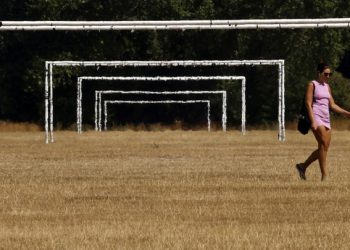 Una mujer pasa junto a las porterías de fútbol de unos campos de juego con el césped seco por el calor, el 13 de agosto de 2022 en el parque de Hackney Marshes, en Londres. Foto: AFP.