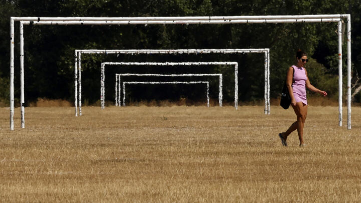 Una mujer pasa junto a las porterías de fútbol de unos campos de juego con el césped seco por el calor, el 13 de agosto de 2022 en el parque de Hackney Marshes, en Londres. Foto: AFP.