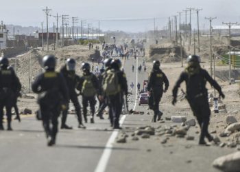 Unos policías avanzan por la autopista Panamericana, cortada por manifestantes con barricadas y piedras para pedir la dimisión de la presidenta de Perú, el 12 de enero de 2023 en Arequipa. Foto: AFP.