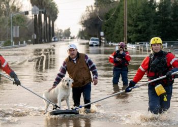 Bomberos de San Diego ayudan a Humberto Maciel a rescatar a su perro de su casa inundada en Merced, California, el 10 de enero de 2023. Foto: AFP.