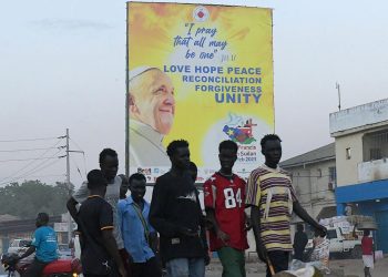Un grupo de jóvenes camina en Juba cerca de un cartel alusivo a la visita del papa Francisco a Sudán del Sur el 31 de enero de 2023. Foto: AFP.