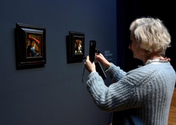 Una mujer fotografía los cuadros del pintor holandés Johannes Vermeer "Mujer joven con sombrero rojo" y "Muchacha con flauta" el 6 de febrero de 2023 en el Rijksmuseum de Ámsterdam. Foto: AFP.